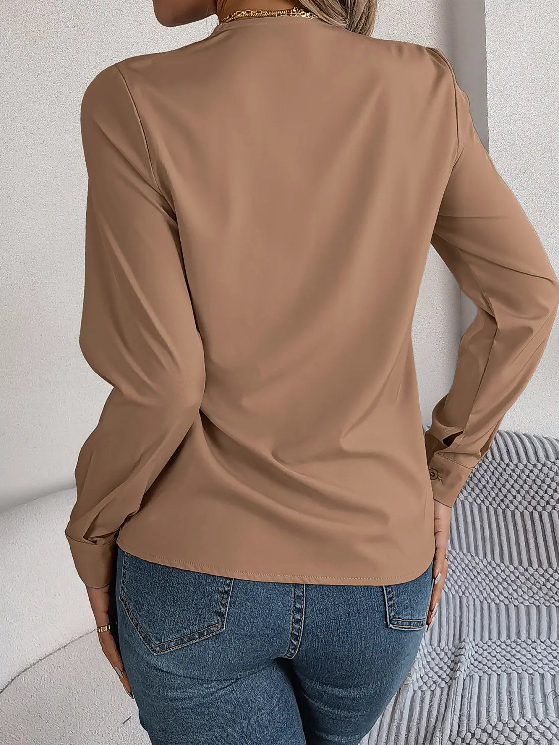 A sleek long-sleeved camel-colored satin blouse with subtle shoulder detailing and black trim v neck wrap design.
