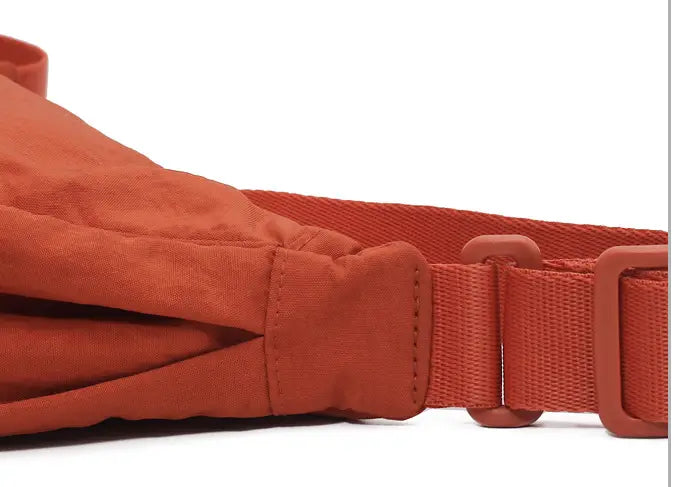 Orange nylon dumpling messenger bag with curved adjustable crossbody strap and plastic buckle for secure fastening.