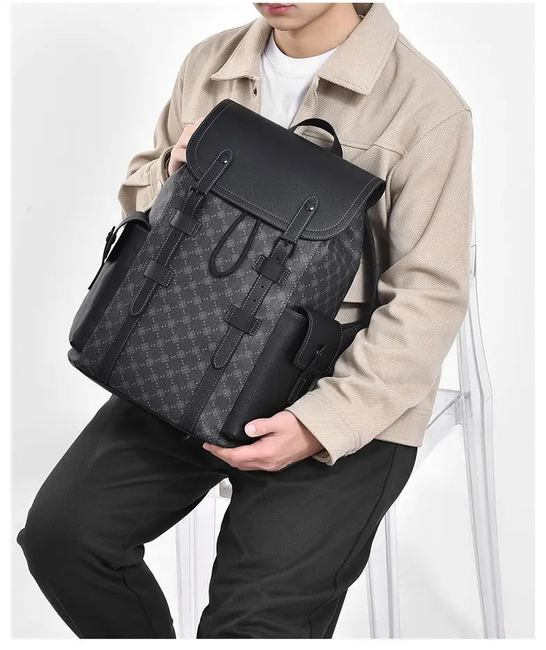 Men’s leather business travel backpack in black featuring a repeating monogram pattern on the main body with solid black leather accents straps and flap including a laptop sleeve.