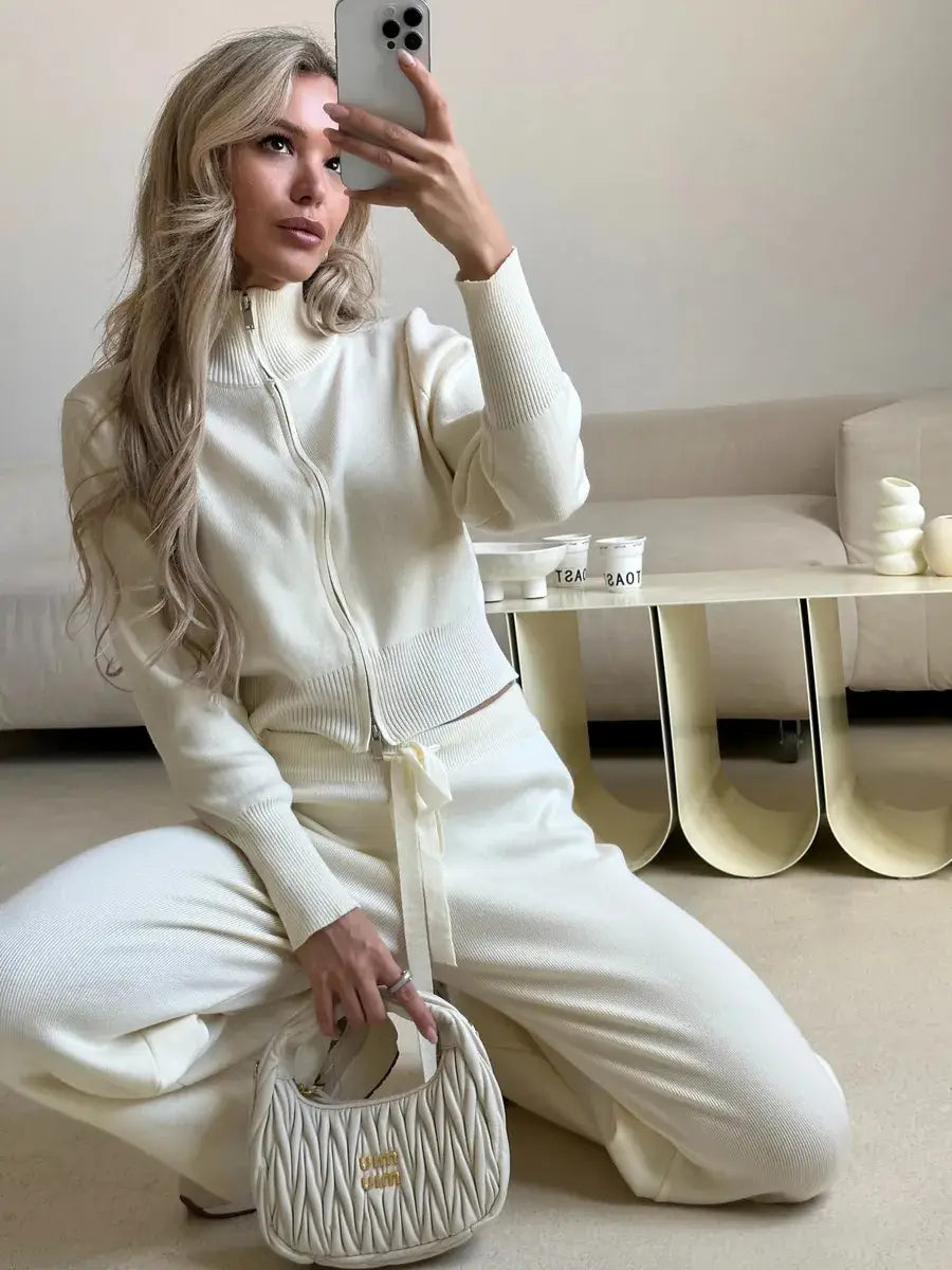 Cream-colored quilted handbag with a gold-tone logo plaque complementing the women’s knit zip up cardigan and wide leg pant set.