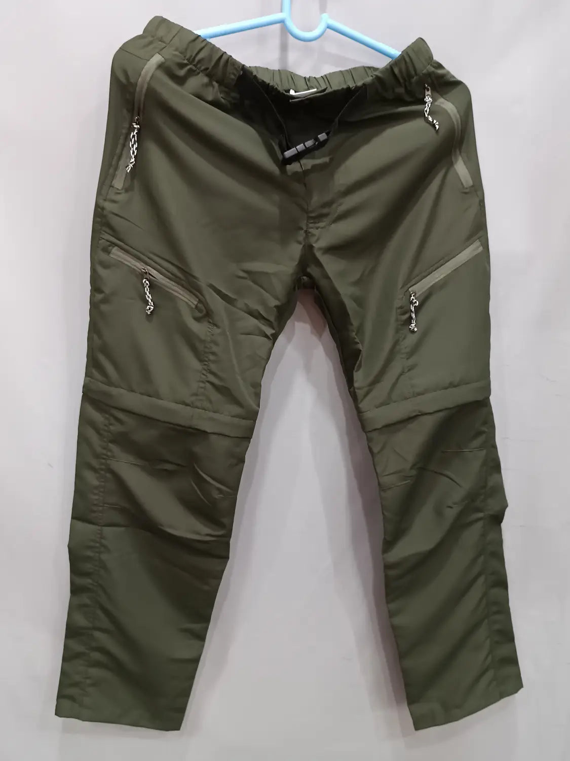 Olive green convertible tactical hiking pants featuring zippered pockets with chain pulls designed for durability and outdoor use.