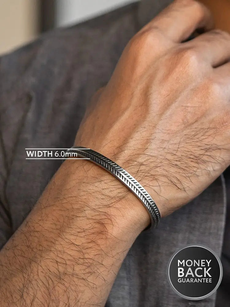 Silver-toned stainless steel cuff bracelet with intricate feather bone and braided edge pattern
