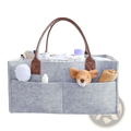 Gray felt baby diaper caddy organizer bag with brown leather handles and multiple compartments holding baby care items