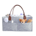 Gray felt diaper caddy nursery storage basket with brown leather handles and multiple compartments holding baby care items