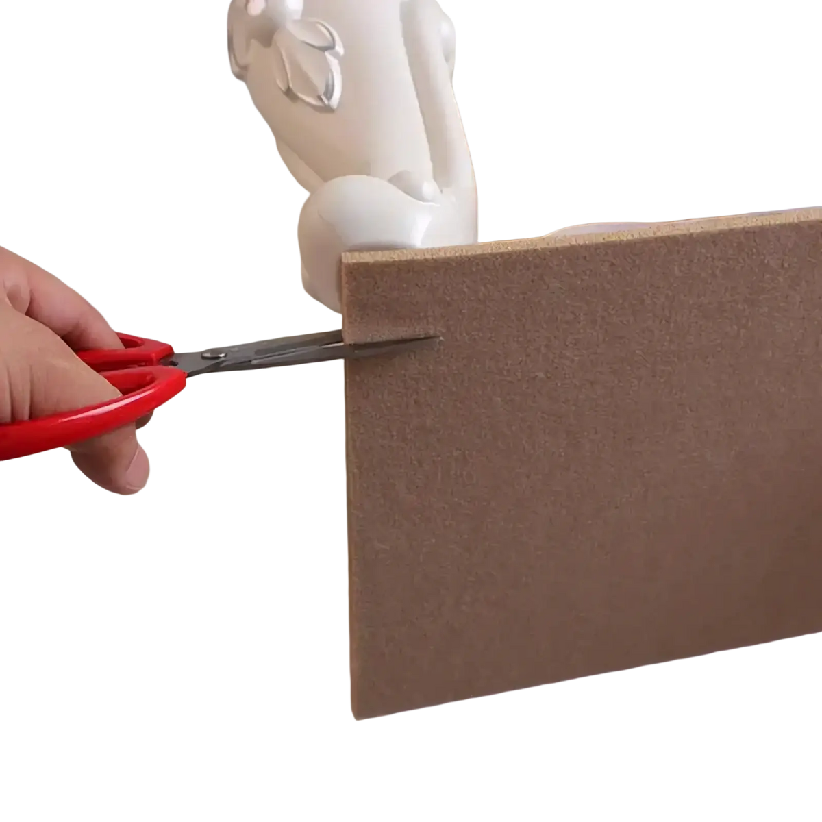 Red-handled scissors cutting a brown textured corkboard panel for felt furniture pads 5mm floor protector use