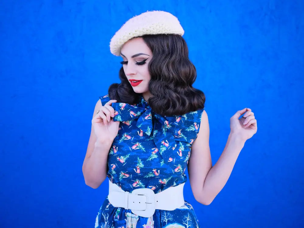 A woman wears a festive fox print vintage bow blouse in blue with a floral pattern and cream knit beret