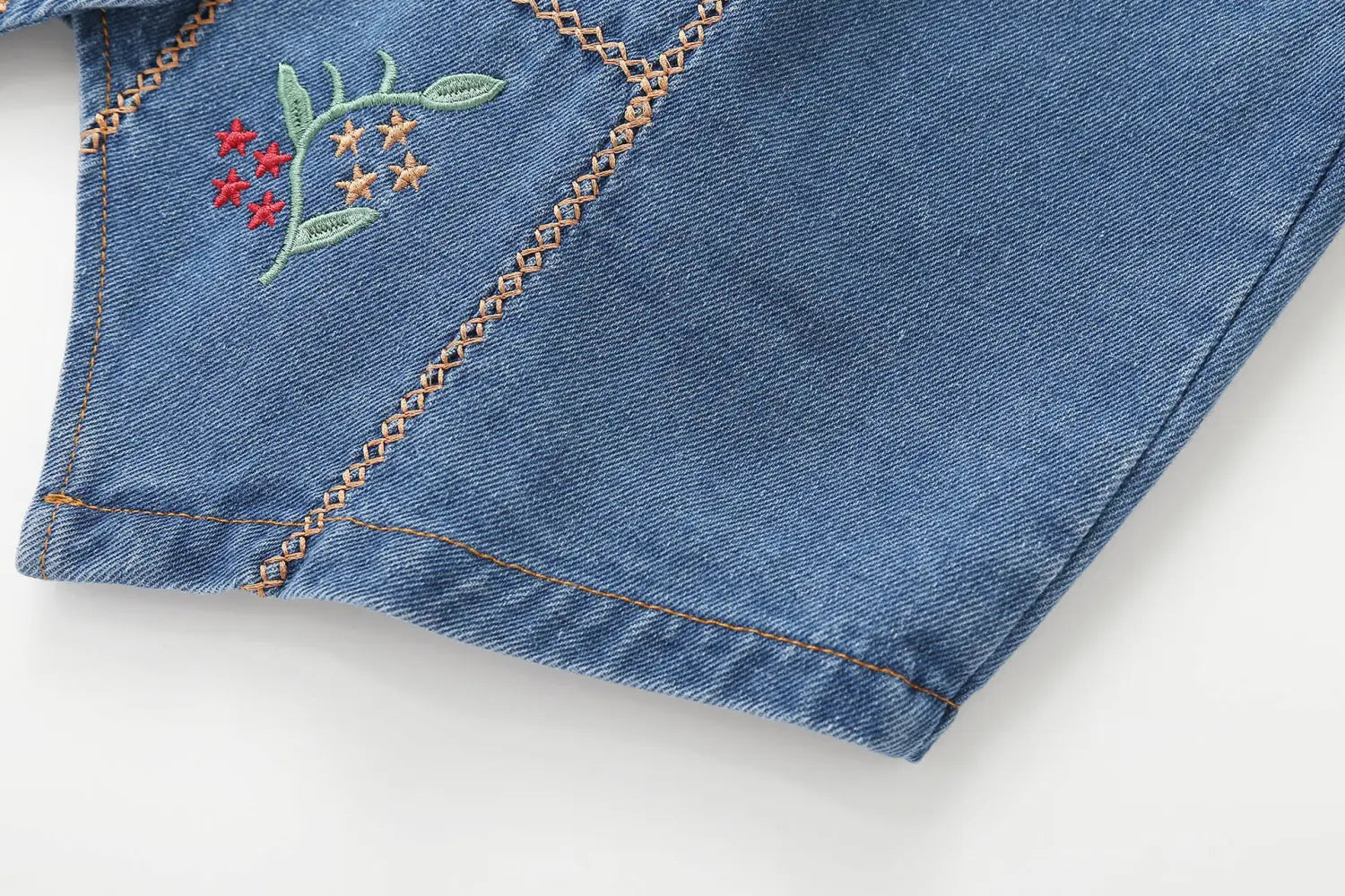 Blaue Jeansshorts mit zartem besticktem floralen Design, mit roten und goldenen Sternen auf grünen Stielen sowie Zickzackstichführung entlang der Naht.