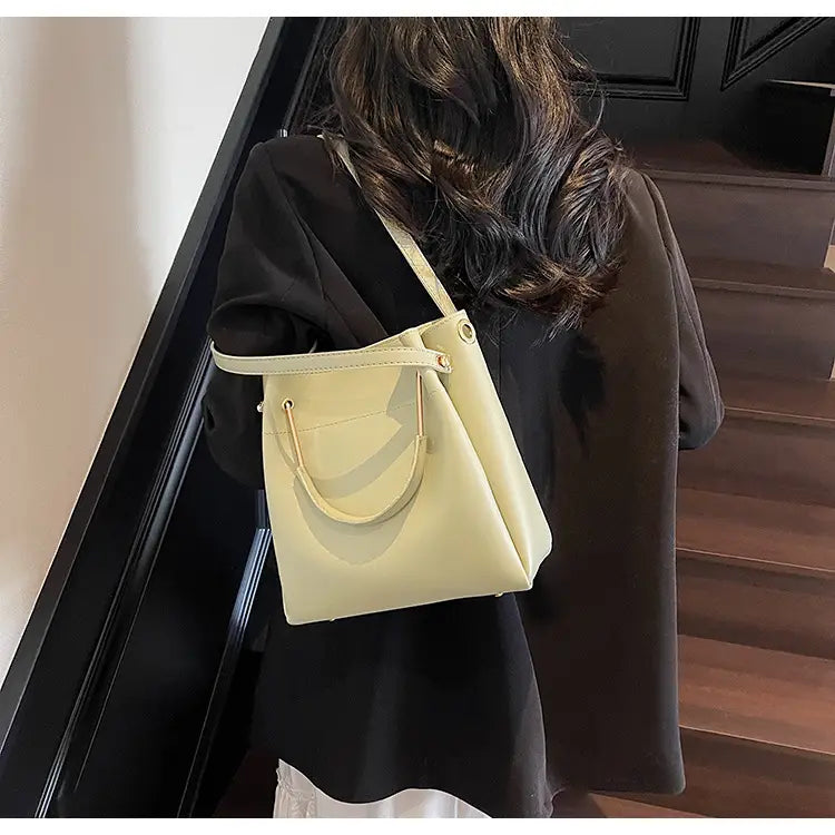 Minimalist leather bucket bag in pale yellow with a structured shape smooth leather-like finish and matching top handles.