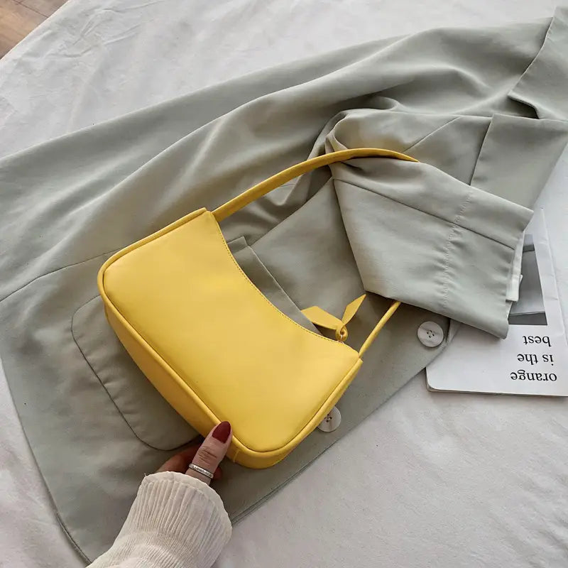 Eine lebhaft gelbe minimalistische Umhängetasche aus Kunstleder mit gebogenem Unterarmgriff, mit einem eleganten Leder-Schultertaschen-Design und passendem Henkel.
