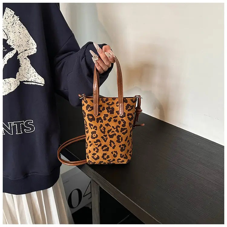A tan and black leopard-print retro suede mini bucket crossbody bag with brown leather handles and an adjustable strap.
