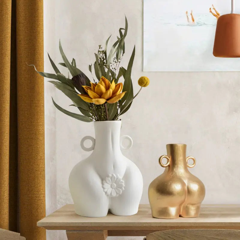 white ceramic female body ceramic vase shaped like stylized buttocks with circular handles and raised floral design on the front