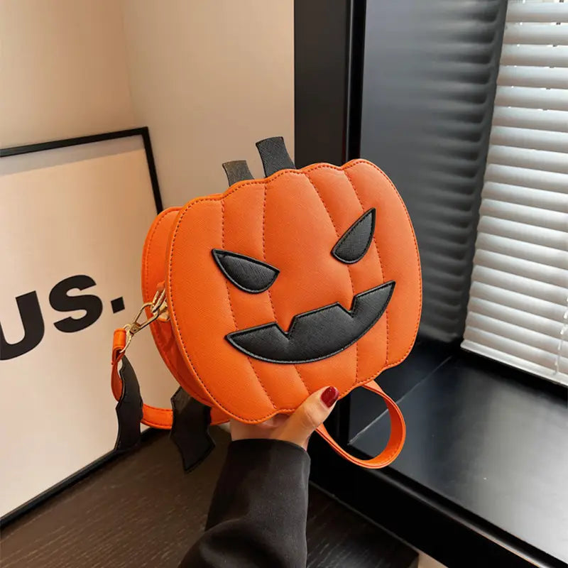 Orange quilted pumpkin-shaped crossbody bag with black stitched facial features and matching strap from the funny pumpkin and bat crossbody bag with detachable charm collection.