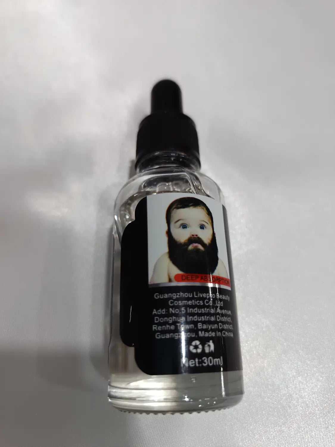 Clear glass bottle with black dropper cap containing 30ml of beard growth oil for natural repair and nourishing care with a label featuring a baby face with a beard.