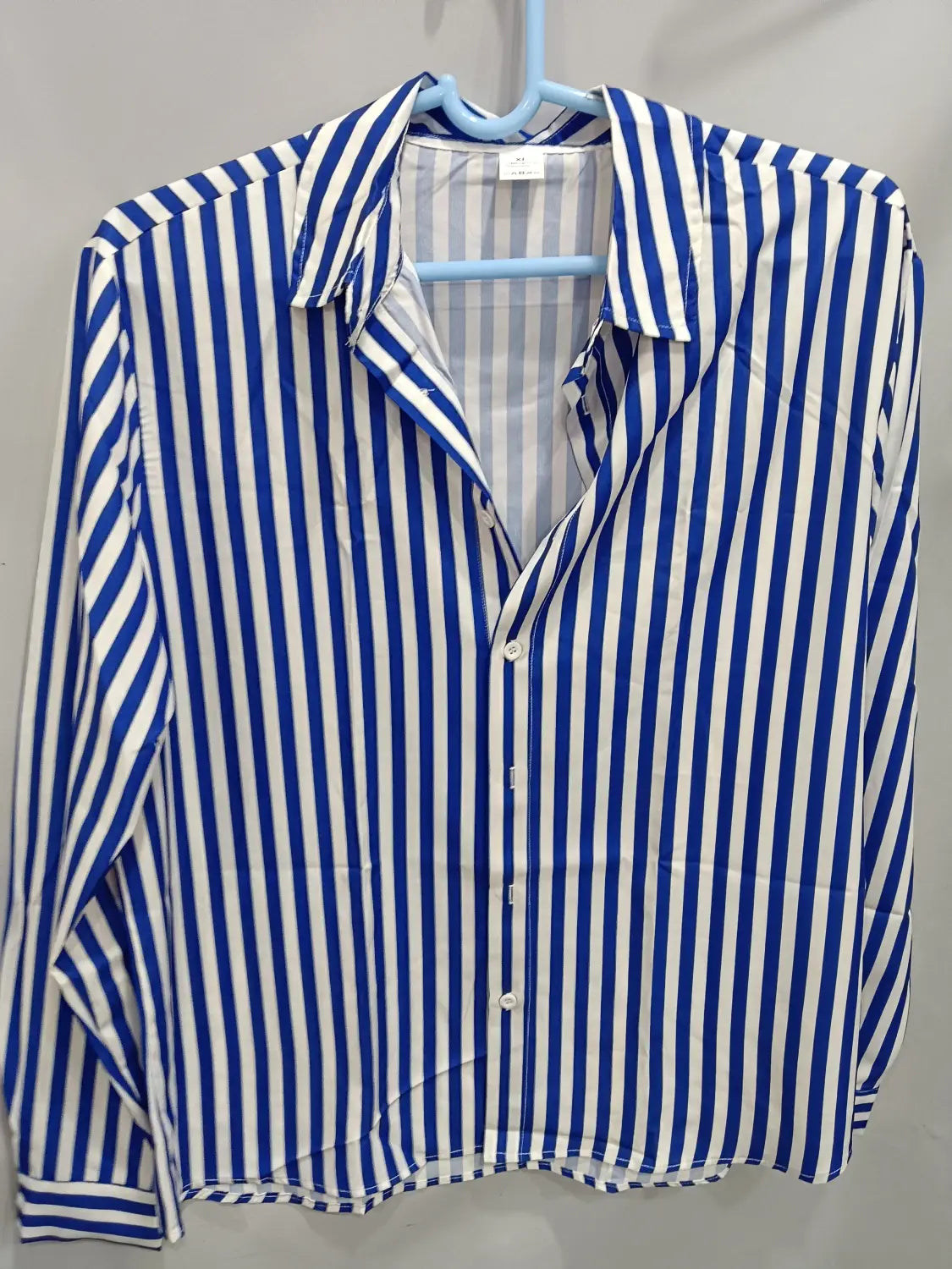 Chemise décontractée à manches longues rayée verticalement bleu et blanc pour hommes, à patte boutonnée et col, suspendue sur un cintre bleu clair.