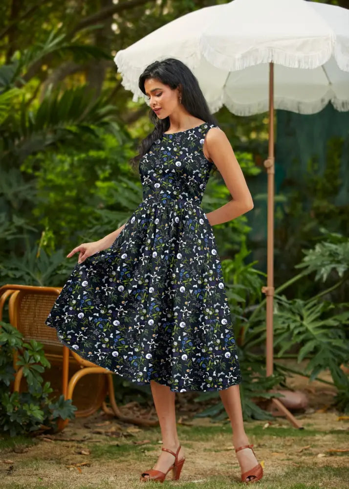 A navy blue floral print cotton sleeveless midi dress with a fitted bodice flared skirt and pockets in 1950s style