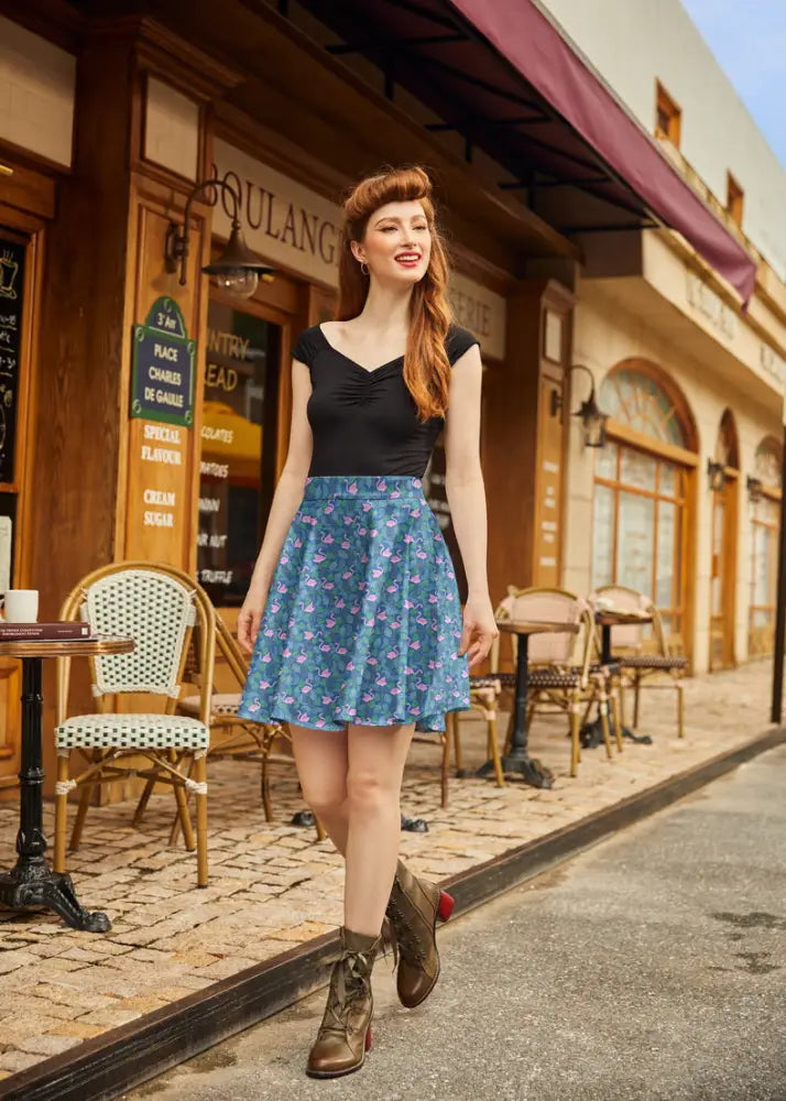 A woman wears a teal flamingo print vintage skater skirt paired with a black top and brown boots