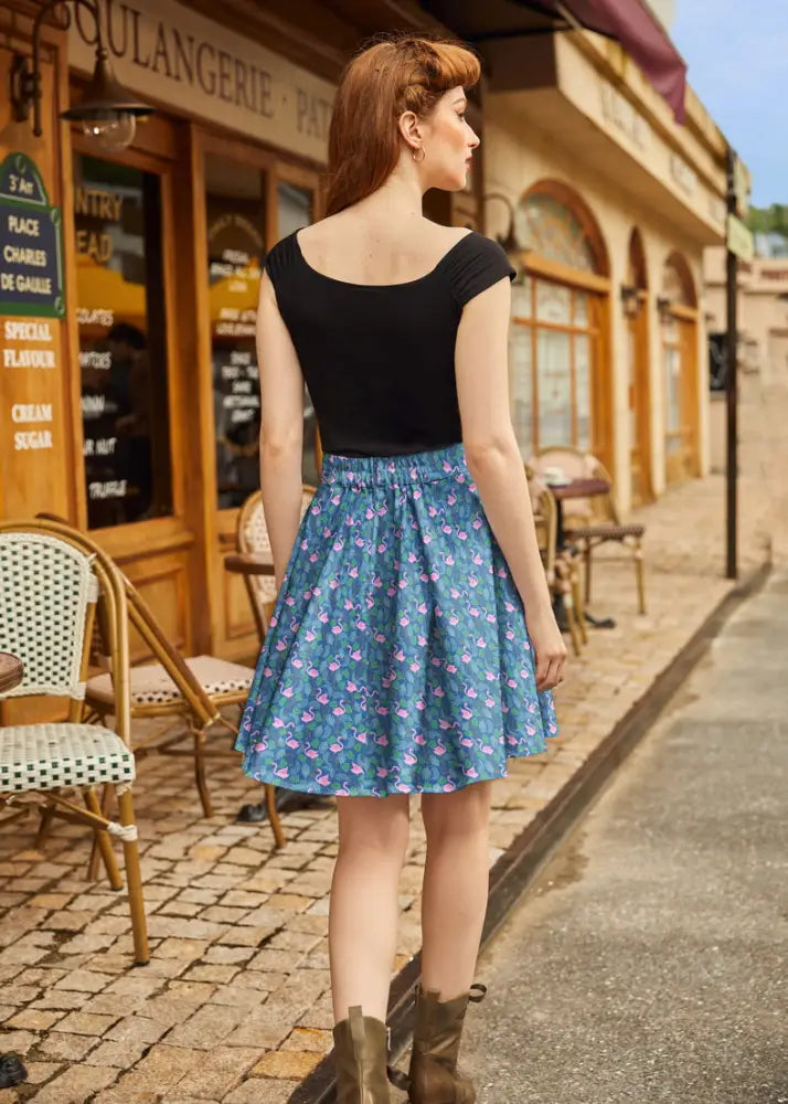 A woman wearing a teal flamingo print vintage skater skirt with elastic waistband paired with a black short-sleeved top