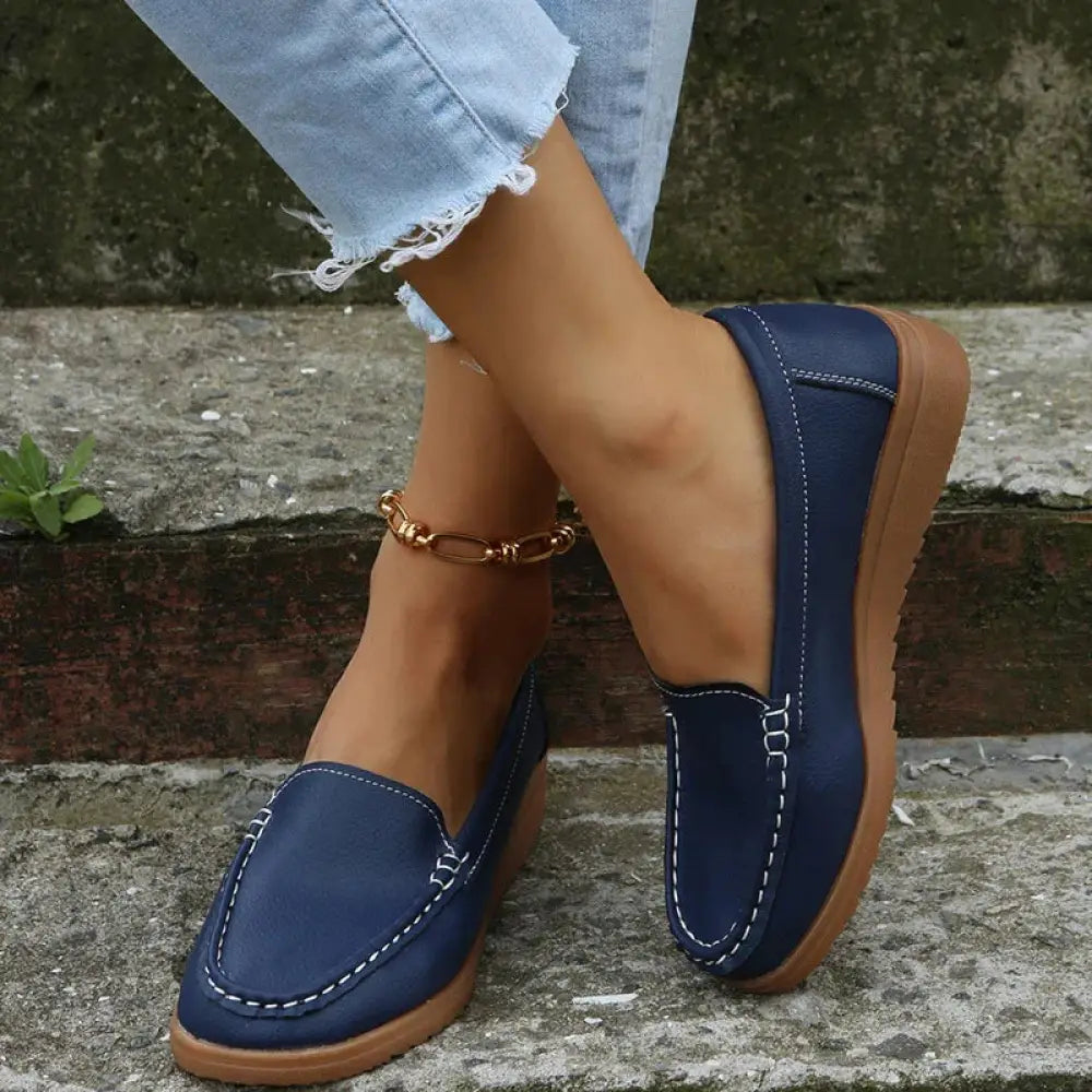 Women’s navy blue pu leather slip on loafers with white contrast stitching and tan rubber sole shown from the back