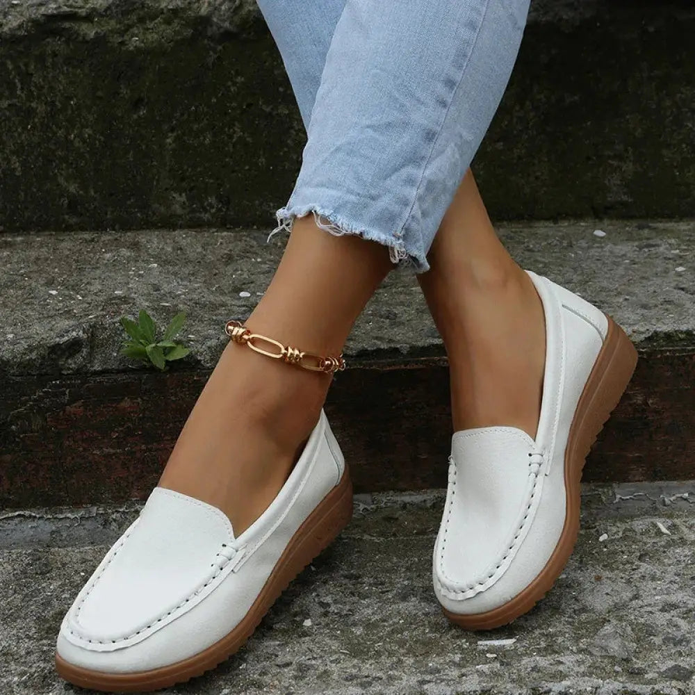 White leather women’s slip on loafers with tan rubber soles and contrast decorative stitching visible from the back side
