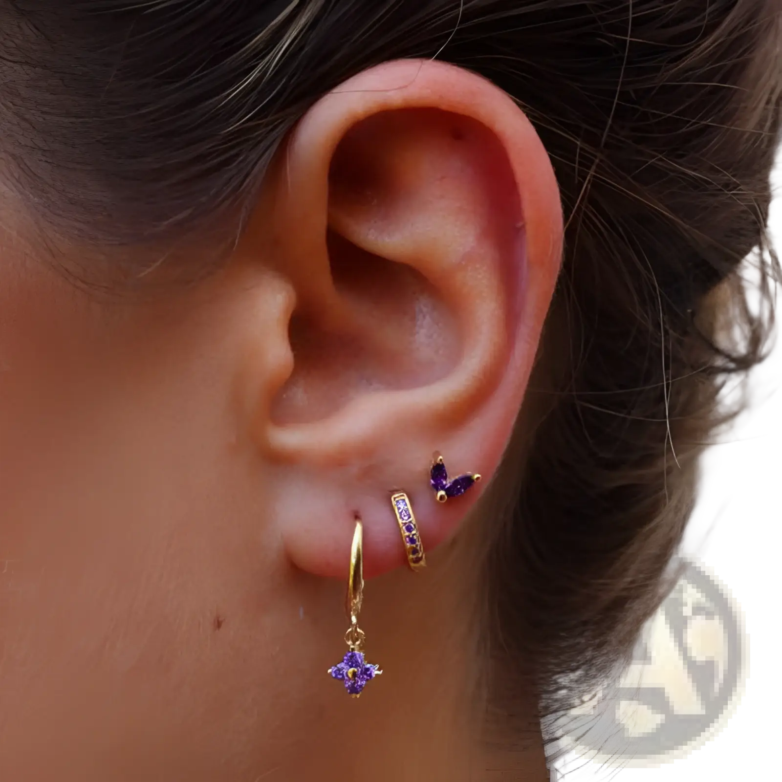 Gold hoop earring set with purple gemstone accents and a dangling flower-shaped pendant in floral and butterfly design