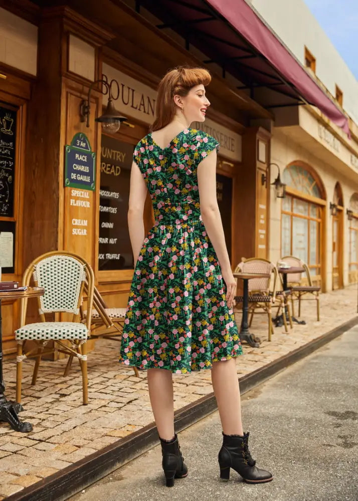 A woman wearing a green floral print floral greta vintage cotton v neck dress with short sleeves and fitted bodice
