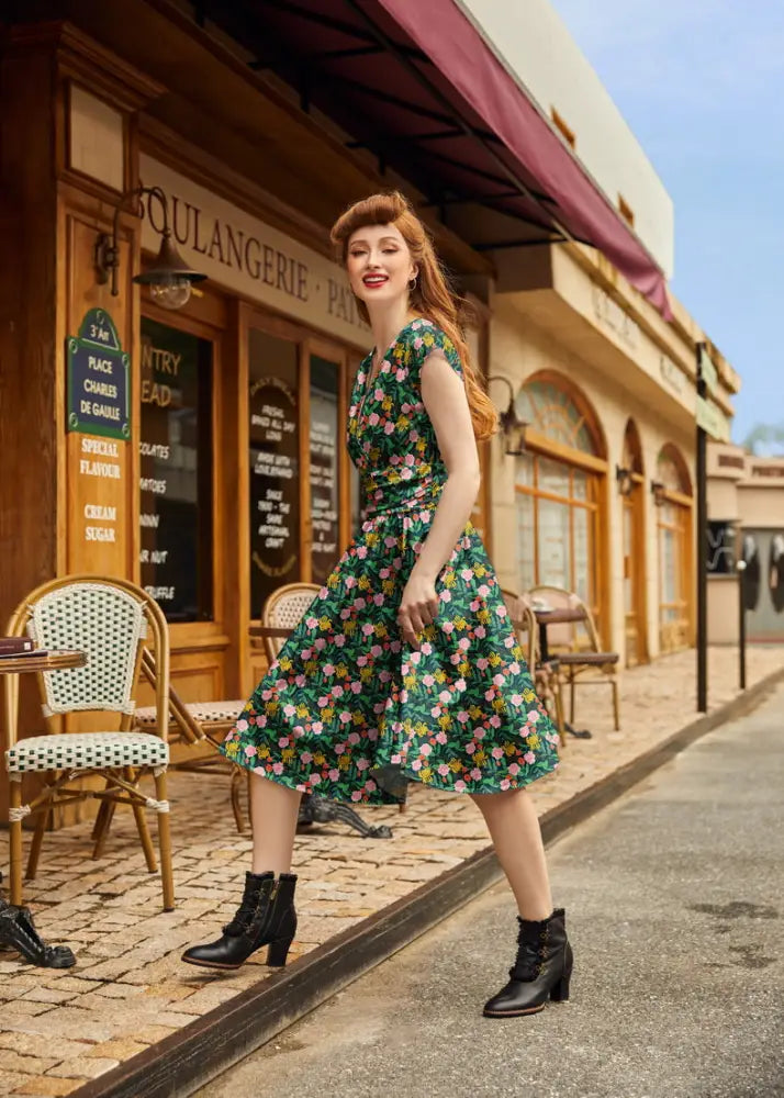 A woman wears a floral Greta green vintage cotton v neck dress with pink and yellow blossoms fitted bodice and flared skirt