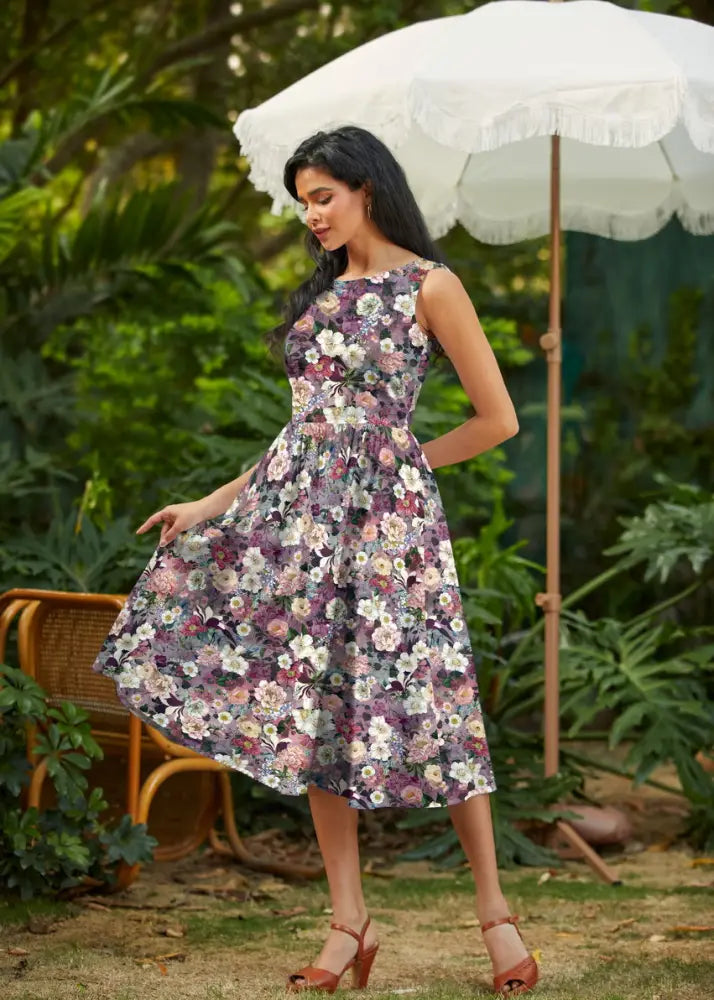A sleeveless vintage floral cotton midi dress with pockets in soft purples and whites featuring a fitted bodice and flared skirt