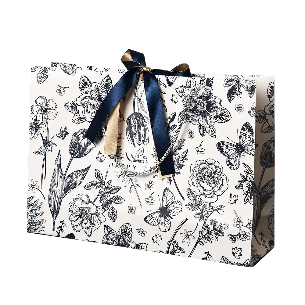 A white paper floral gift bag with black botanical illustrations tied with a navy blue satin ribbon