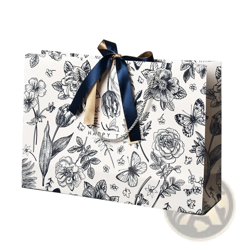 A white paper floral gift bag with black botanical illustrations tied with a navy blue satin ribbon