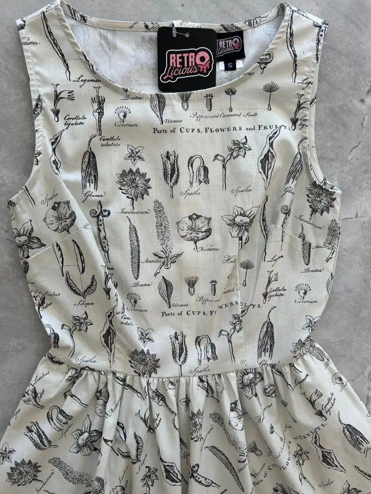 A cream sleeveless cotton a-line dress with black botanical print labeled parts of cups flowers and fruits by Retro Liquor
