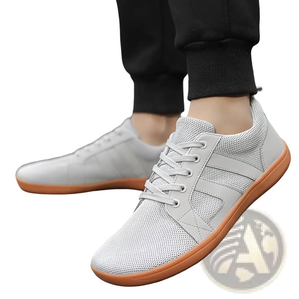 Light gray fly-knit wide last sneakers featuring breathable mesh, orange rubber soles, and matching laces