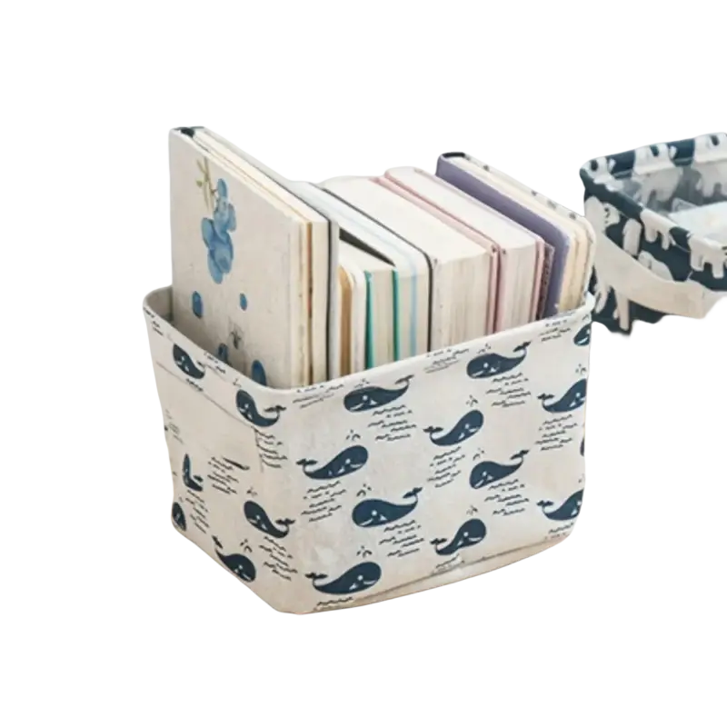 White foldable fabric storage basket with navy blue whale and script print holding stacked notebooks storage box