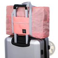 Pink foldable travel duffle bag with gray straps and front zippered pocket made of lightweight nylon for travel convenience