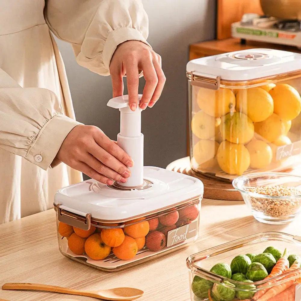 Arbaglobal white plastic vacuum sealer used on clear glass food storage container filled with oranges and red fruits