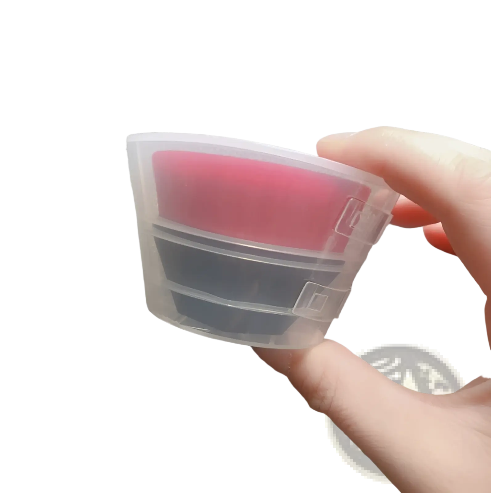 Transparent plastic container holding two stacked silicone pads in pink and dark gray for foundation brush and powder set