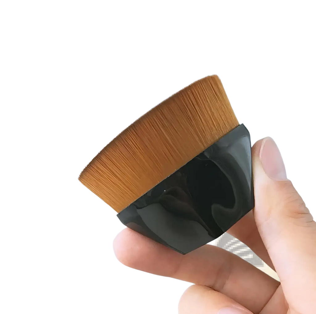 A sleek black-handled foundation brush with dense golden-brown bristles in a powder makeup set with case