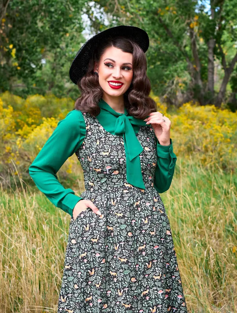 A woman wears a green long-sleeved Foxy Vintage fit and flare dress with a nature print skirt featuring animals and mushrooms