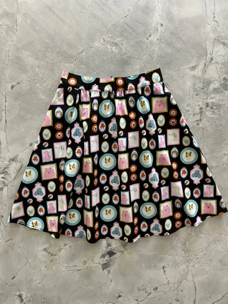 A black cotton vintage a-line skirt with pink and blue cartoon dog pattern framed in gold trim with pockets