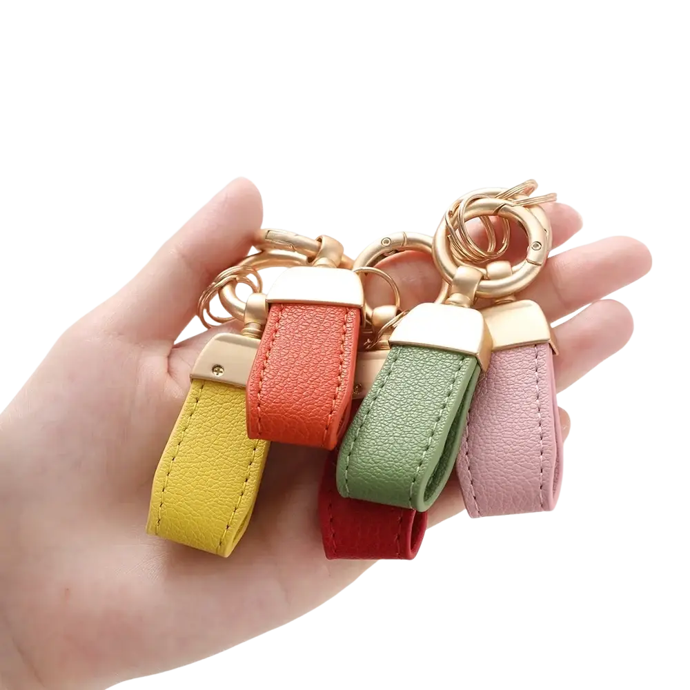 A hand holds four colorful french sheepskin leather car key chain pendants with gold-tone rings in yellow orange green and pink