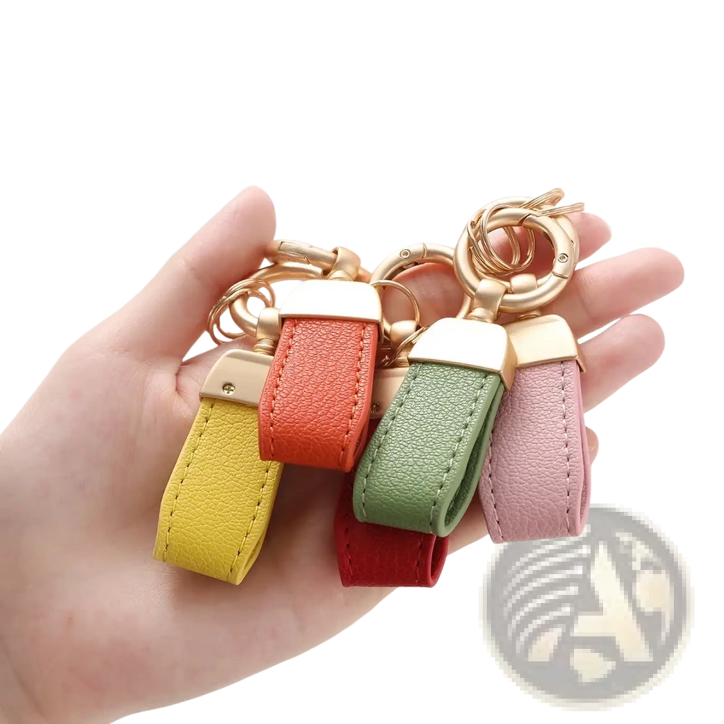 A hand holds four colorful french sheepskin leather car key chain pendants with gold-tone rings in yellow orange green and pink