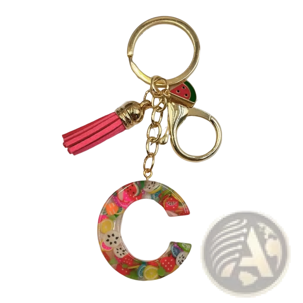 A vibrant transparent acrylic fruit letter c keychain with gold metal accents and a pink tassel for keys or bags