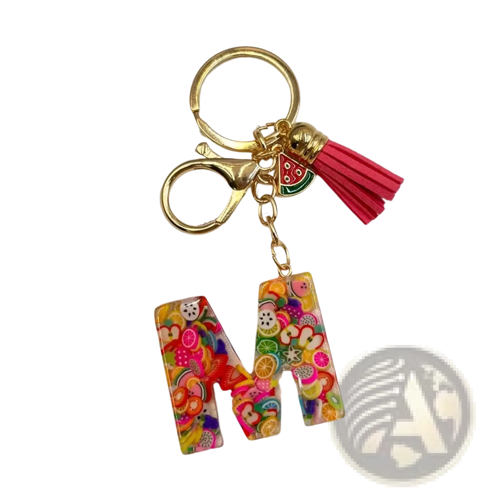 A vibrant transparent resin keychain shaped like letter m with colorful fruit slices gold ring and pink tassel