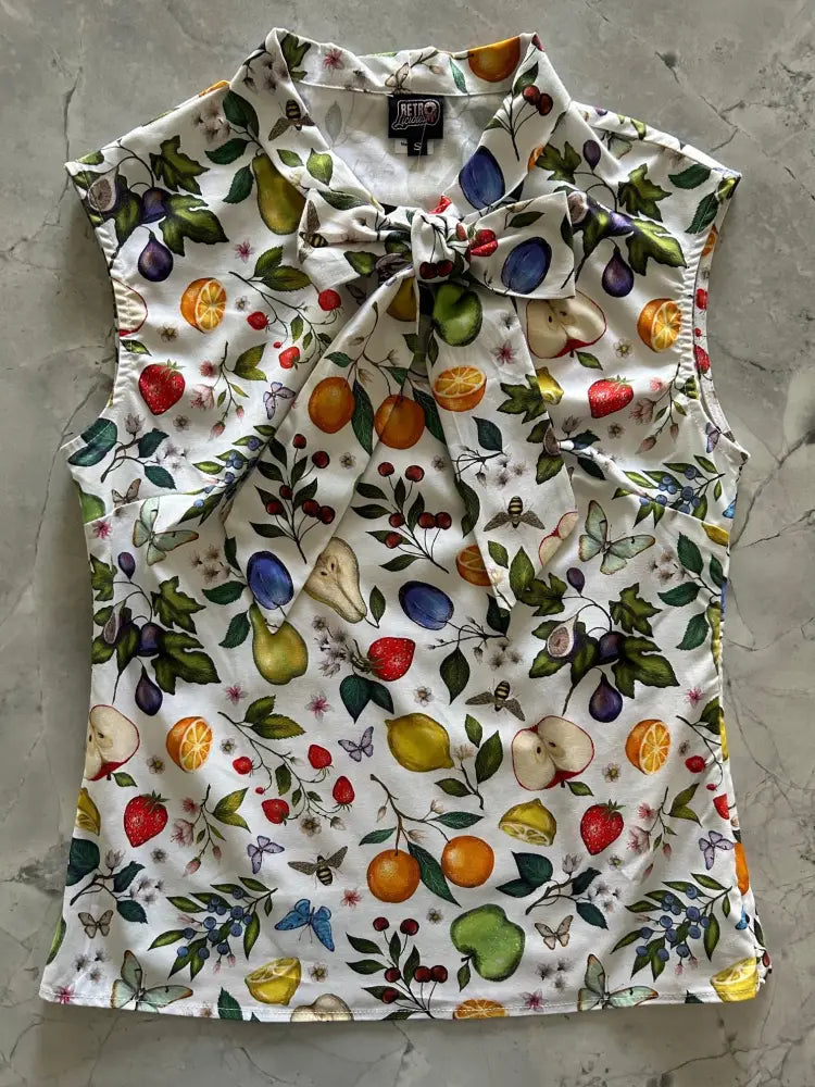 A white sleeveless vintage 1950s cotton blouse with vibrant fruit and butterfly print and a tied bow collar
