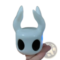 Glossy white ceramic hollow knight figurine with black eyes and horn-like protrusions game controller stand display
