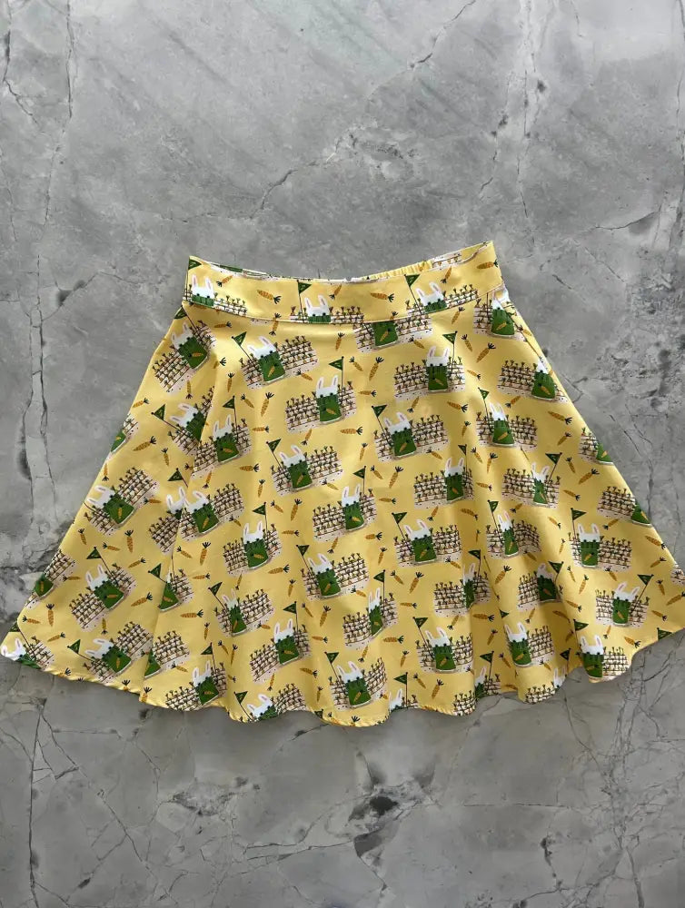 Yellow cotton skater skirt with green frogs wearing white hats and brown fences in playful garden pattern
