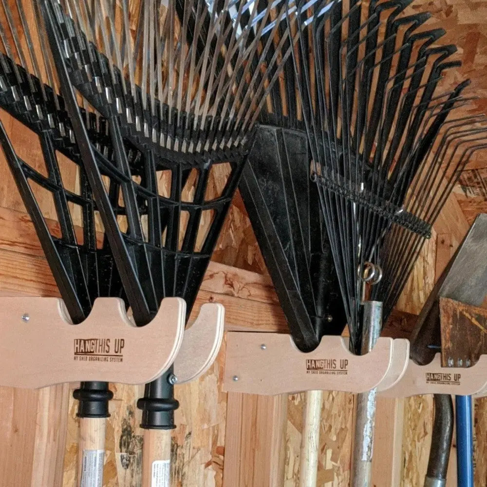 Stud mounted wave design wooden garden tool organizer with black plastic rake heads and wooden handles on light wood racks