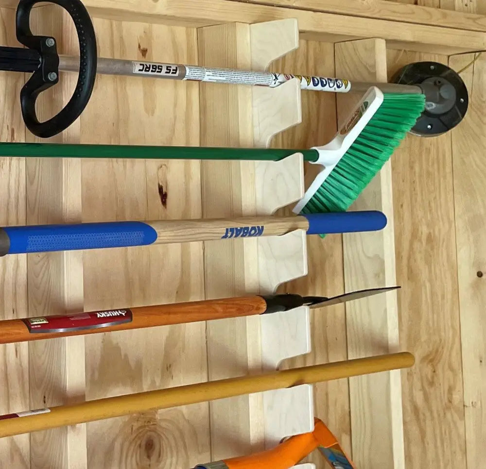 Birch wood stud mounted garden tool organizer rack holding a green bristled broom with white handle and blue grip
