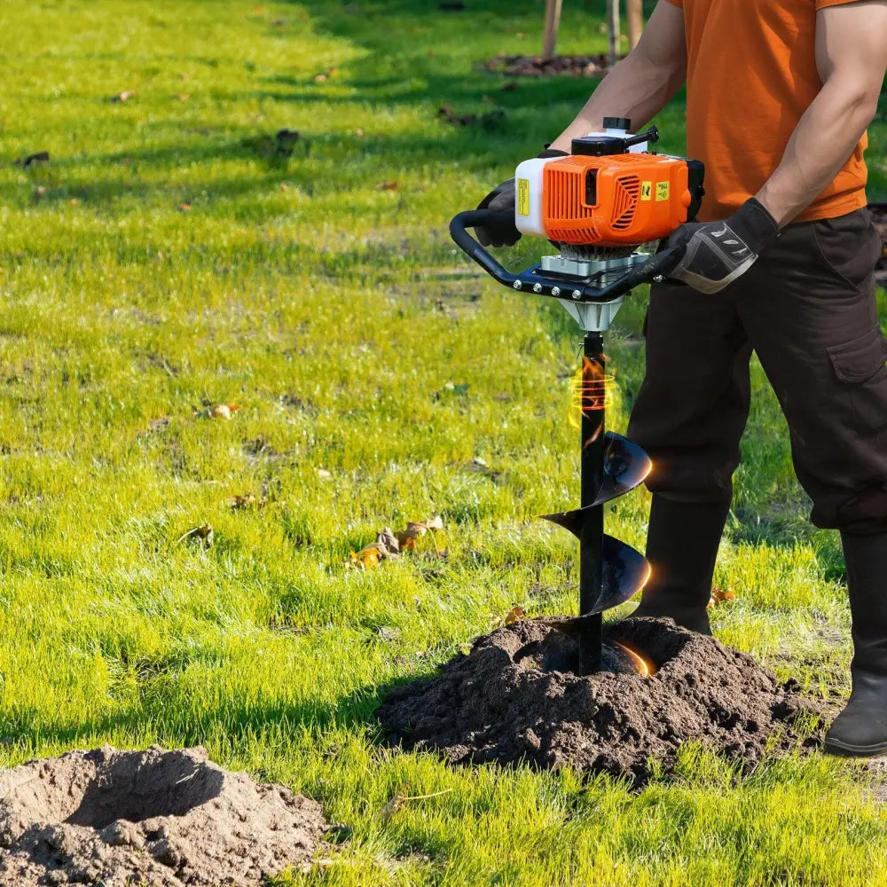 Orange and white 63cc gasoline-powered gas post hole digger with black spiral bit digging into grassy ground