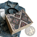 A beige canvas tote bag with vibrant black white pink and blue geometric embroidered pattern for casual commuting
