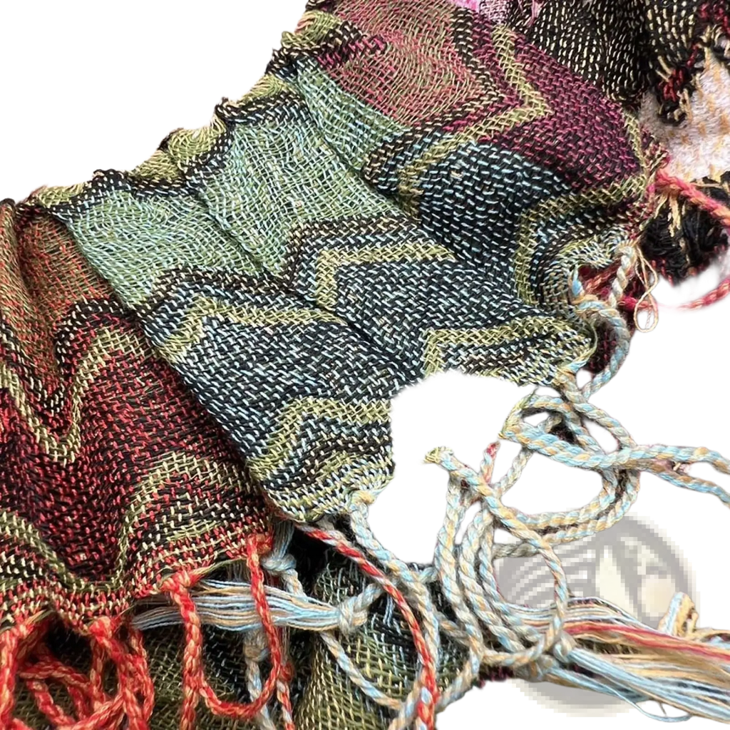Geometric knit scarf with zigzag pattern in earthy green black and rust tones featuring red fringe tassels and frayed edges